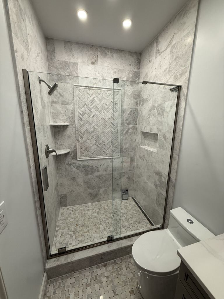 Walk-in shower with large marble wall tile, a herringbone niche, a glass enclosure, and a mosaic floor.